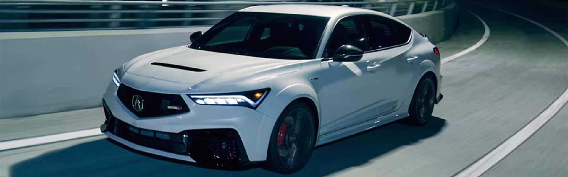 A sleek white car, the 2025 Acura Integra, speeds around a curve on a night-lit road.