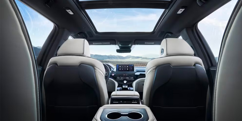 View from the rear seats of a modern 2025 Acura MDX with a sunroof, dashboard, and cup holders.