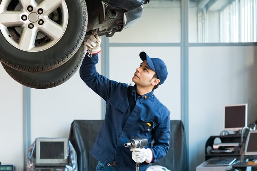 A mechanic examining a raised car wheel using tools in an auto shop.
