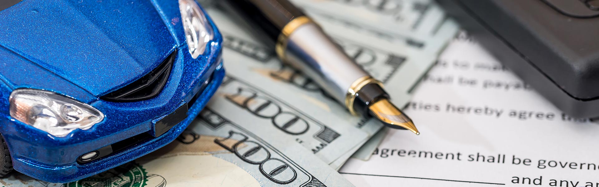 A blue toy car on top of cash, a pen, and a document with text.