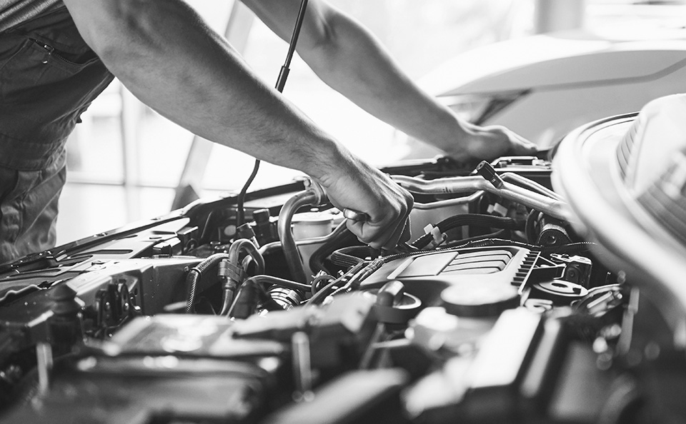 A mechanic is working on a car engine with tools in hand.