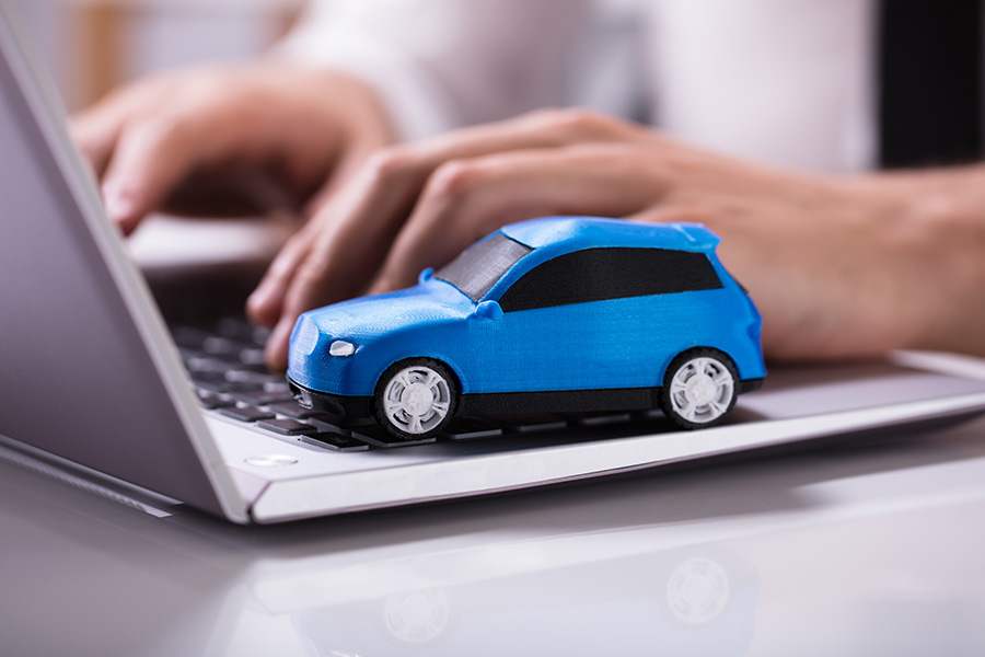 A blue toy car sits on a laptop keyboard while a person types with one hand.