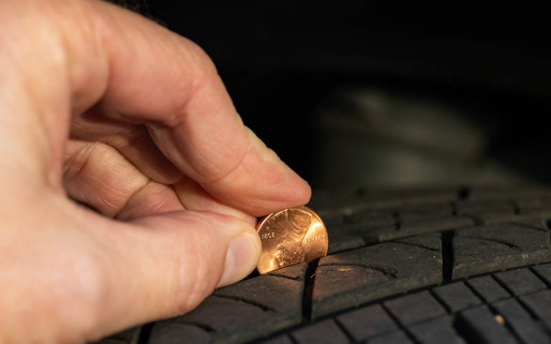 A hand holding a penny, checking the tread depth on a tire.